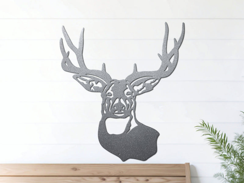 Silver deer head metal wall art hangs on a white wall above a wooden bench